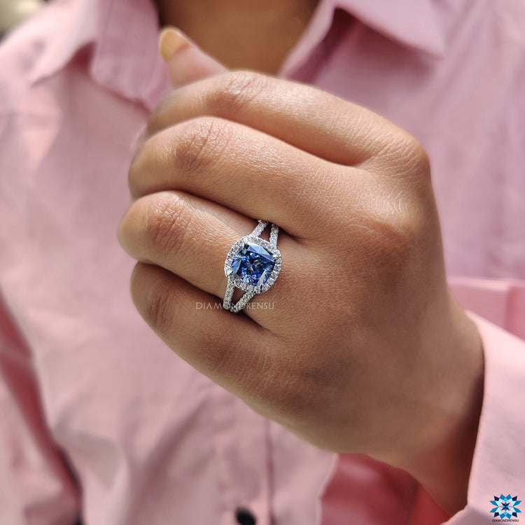 White gold engagement ring with dark blue cushion moissanite and split shank pave band.