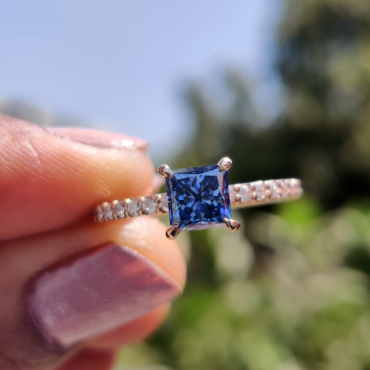 Princess cut moissanite ring with royal dark blue center stone in rose gold setting.