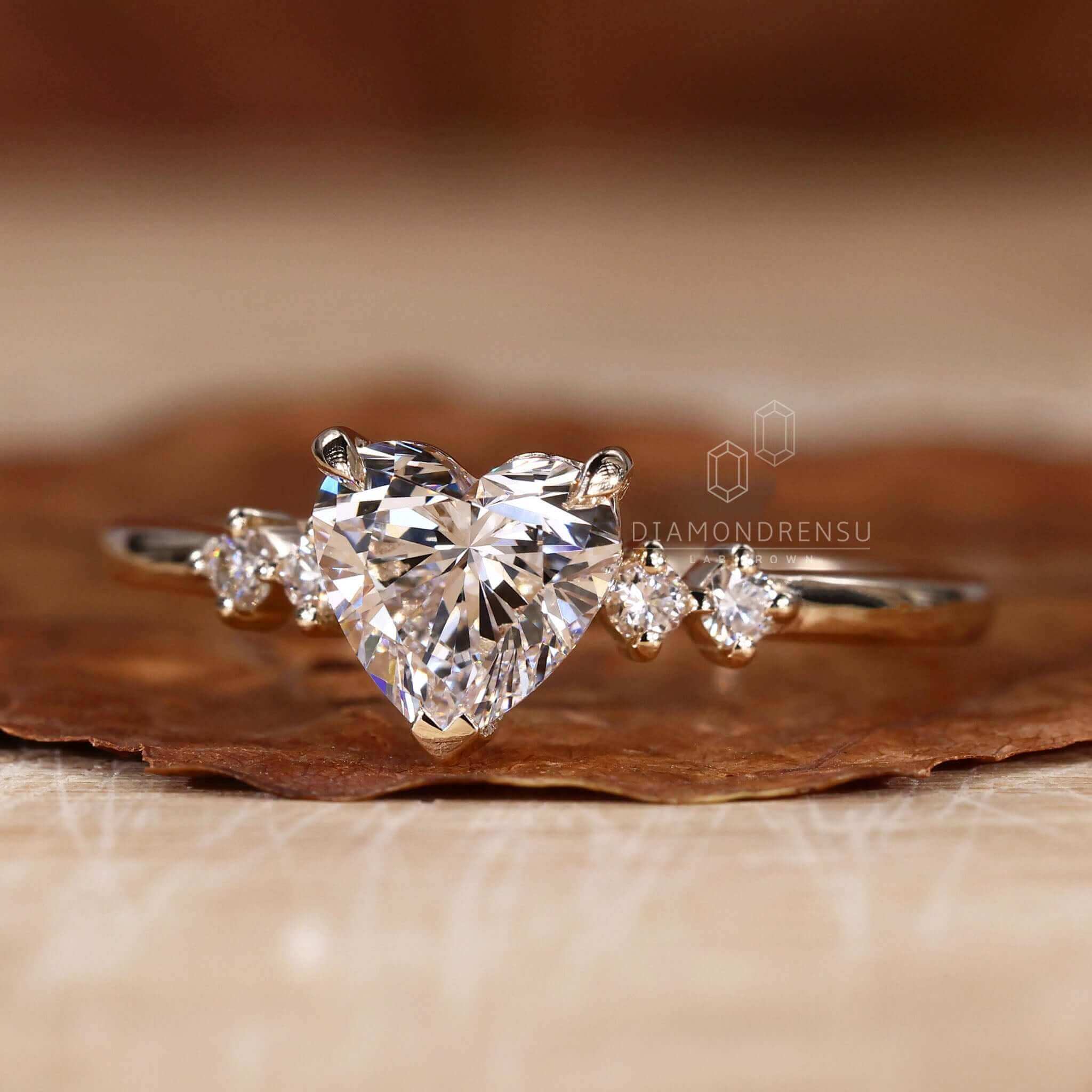Side stone engagement ring with a heart shaped centrepiece and V prong setting.