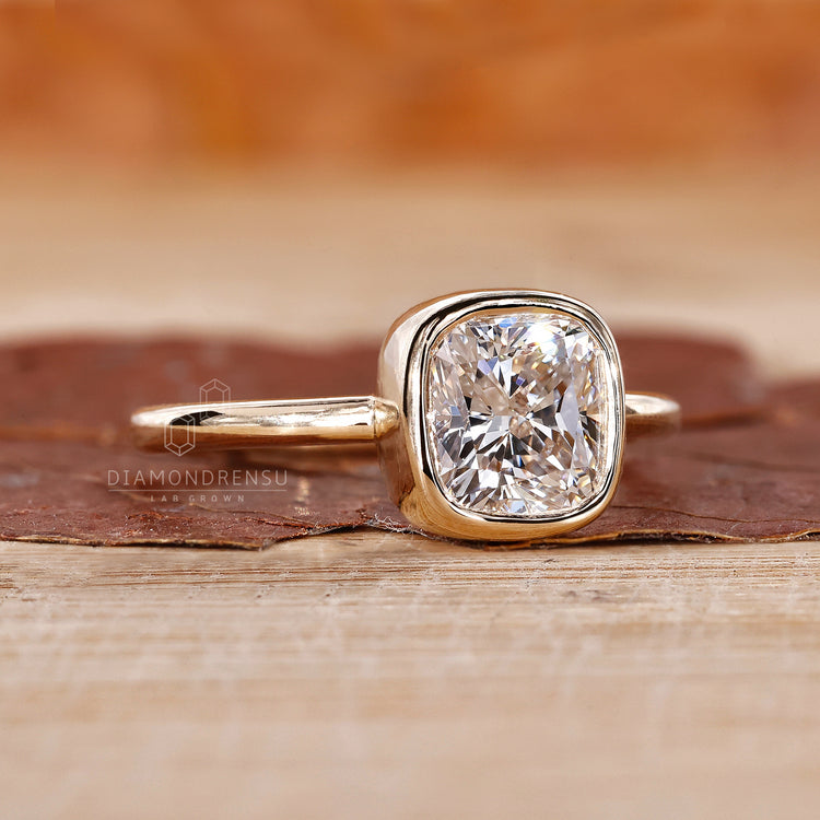 Unique engagement ring features cushion diamond in a bezel setting.