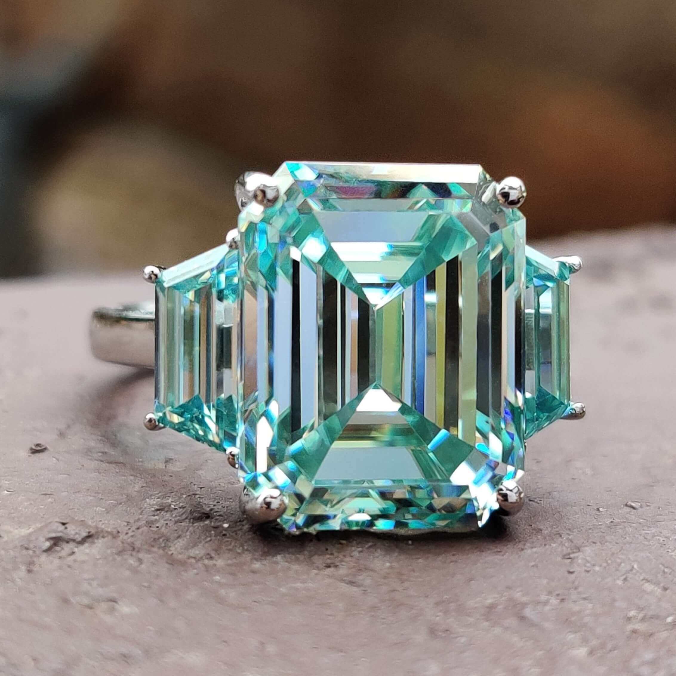 Emerald cut cyan blue moissanite ring in three stone design.