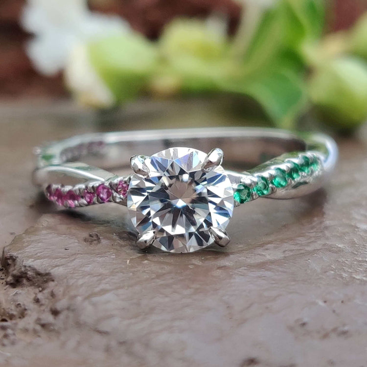 Round cut moissanite ring with ruby and emerald side stones.