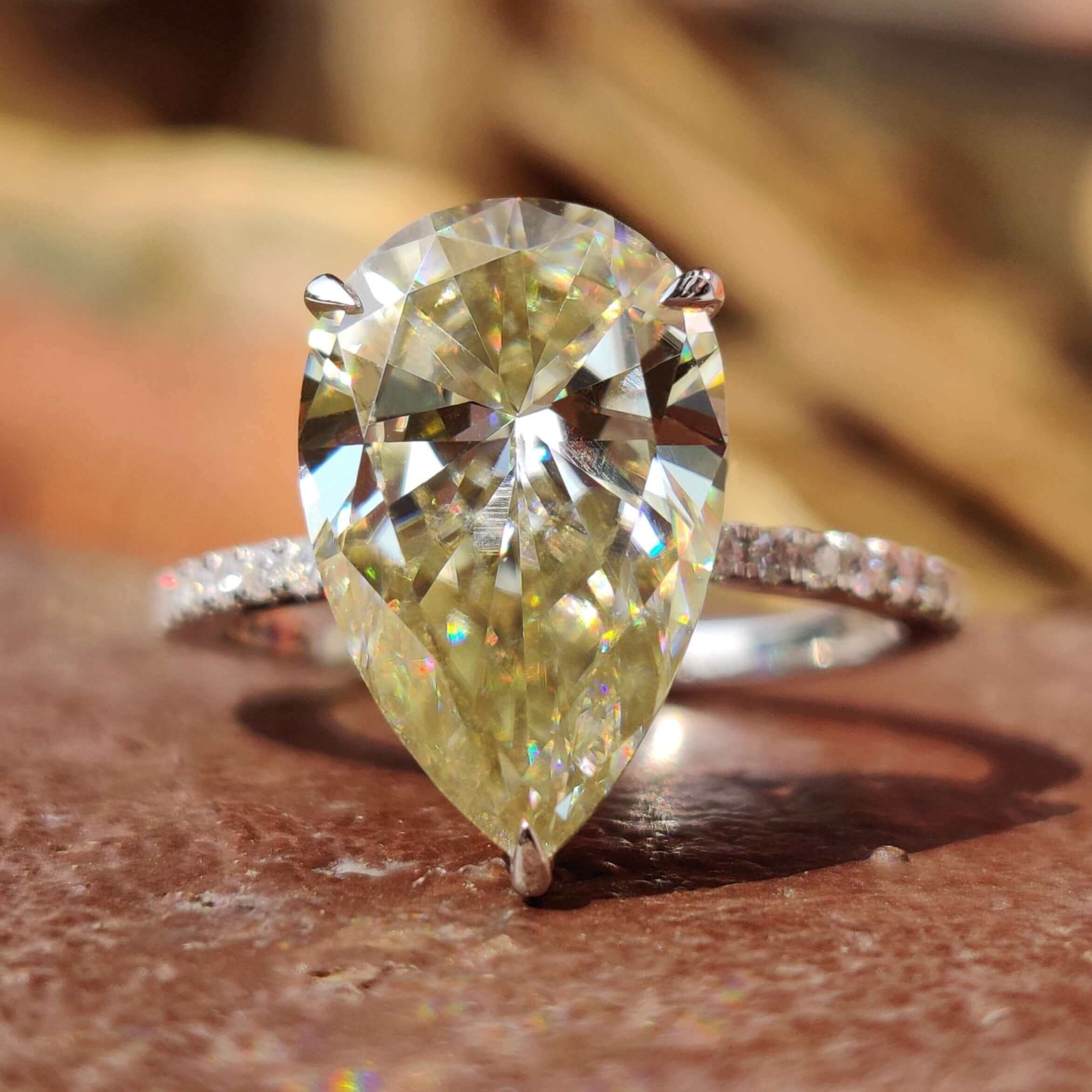Light yellow pear cut moissanite engagement ring with round side stones.