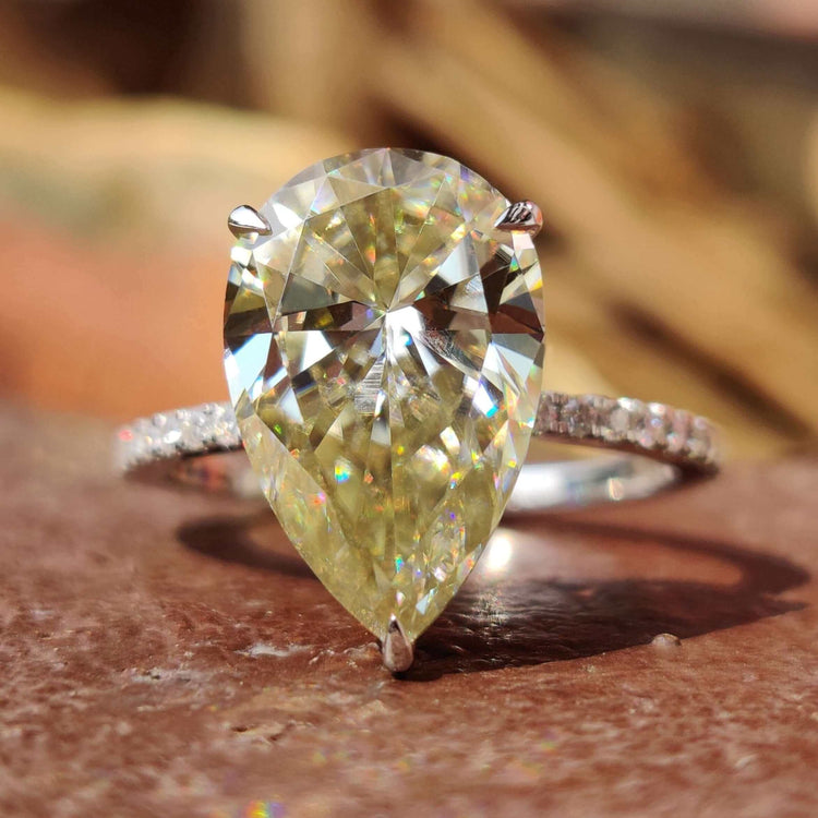 Light yellow pear cut moissanite engagement ring with round side stones.