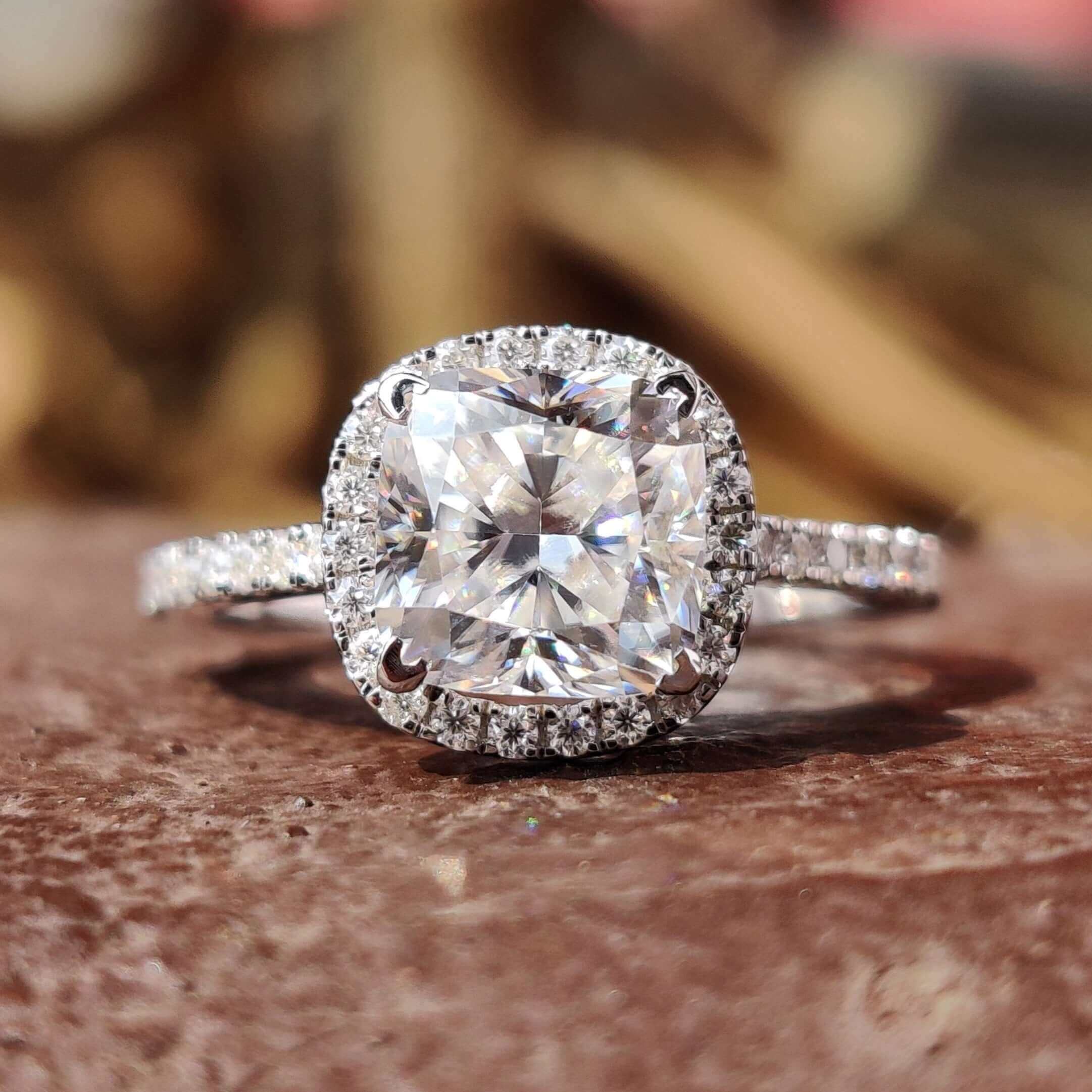 Cushion cut moissanite engagement ring with halo and round side stones.