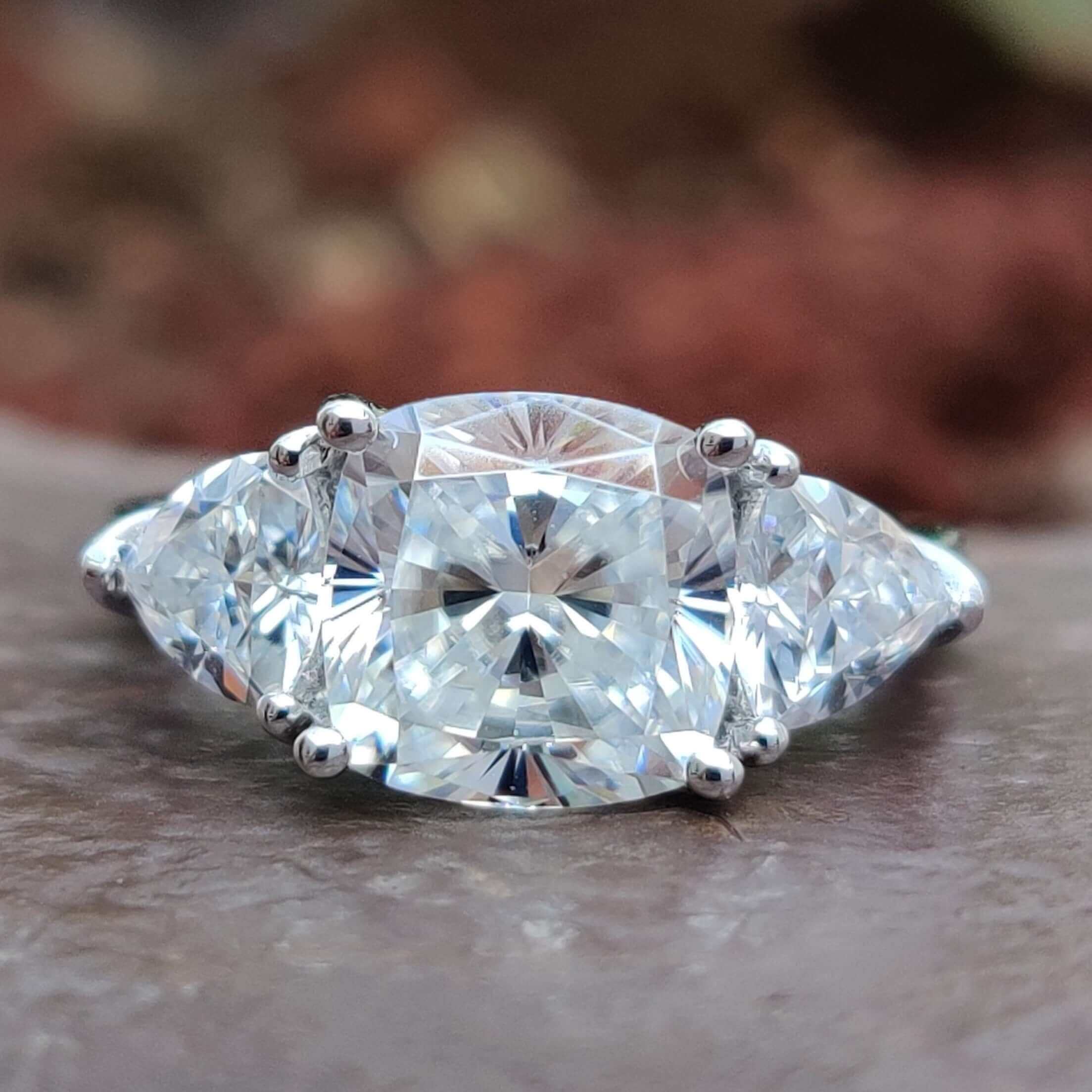 Three stone moissanite ring with cushion cut center and trillion side stones.