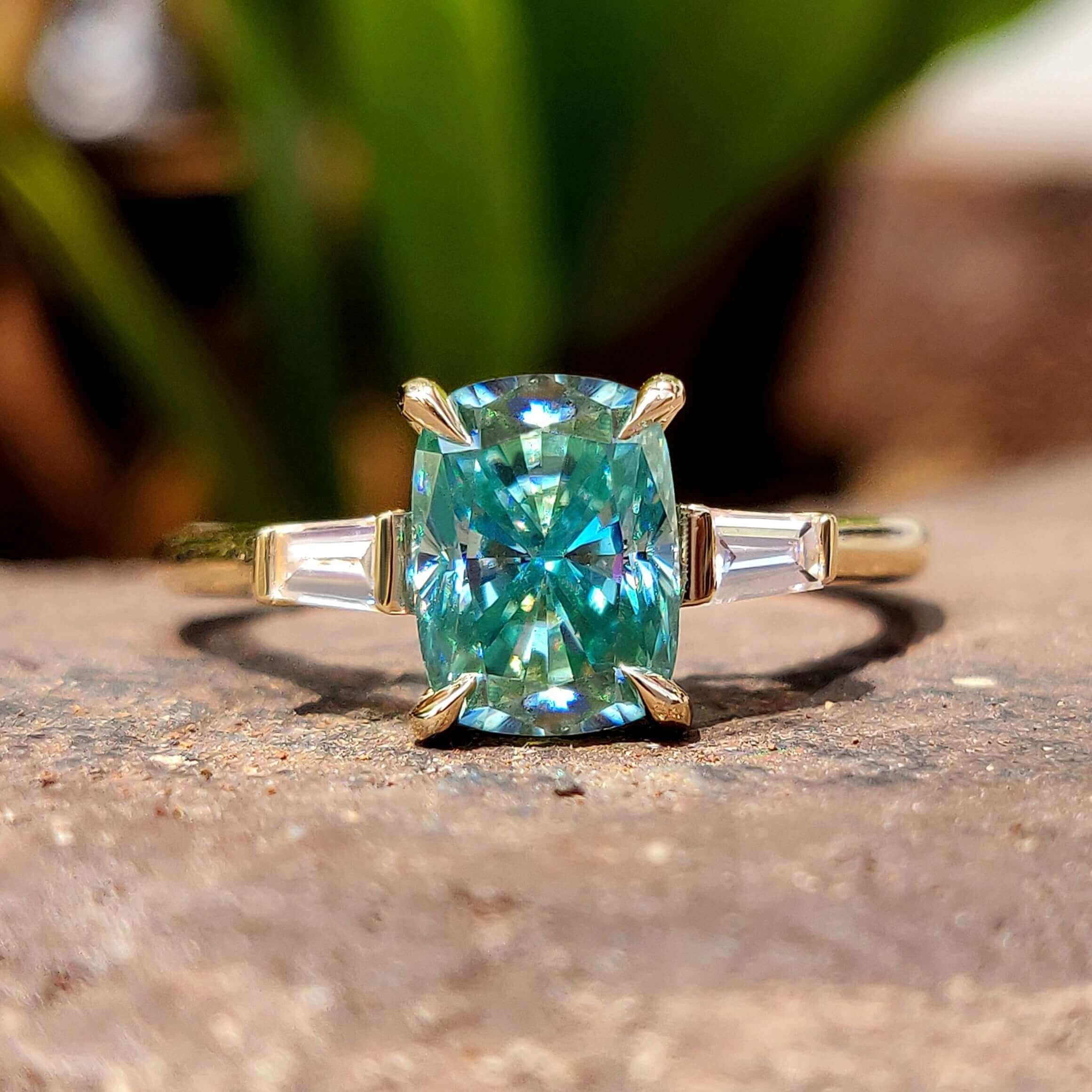 Cyan blue moissanite three stone engagement ring in yellow gold.