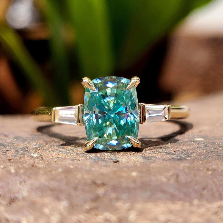 Cyan blue moissanite three stone engagement ring in yellow gold.