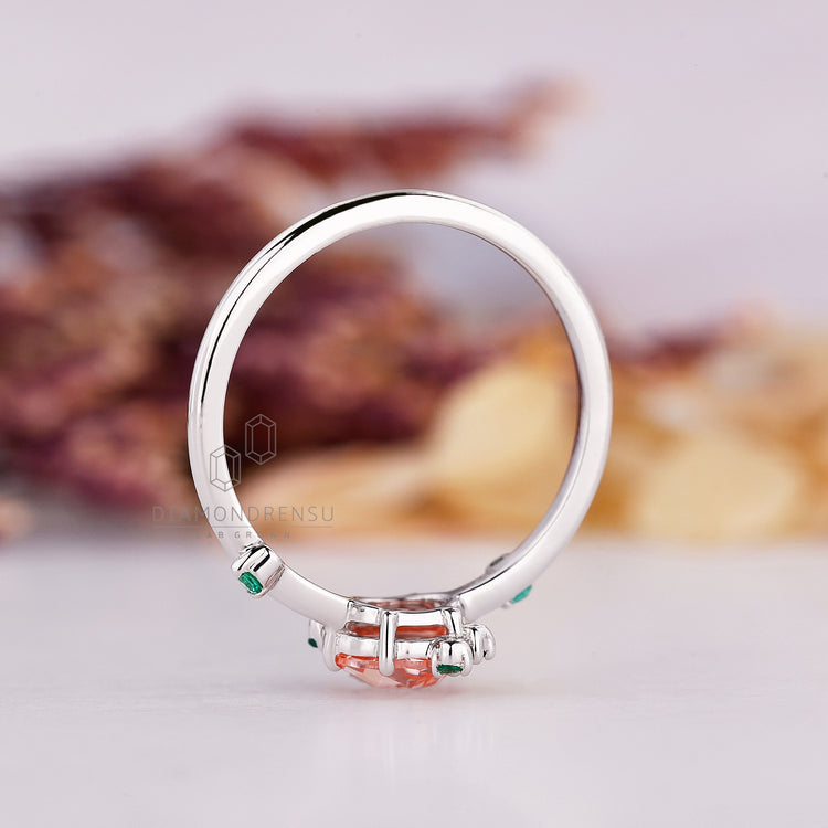 Diamondrensu peach sapphire ring with emerald cluster setting.