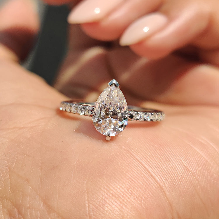 Pear shaped engagement ring with claw prong and moissanite pave band.