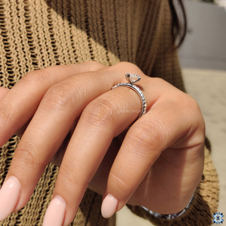 Moissanite engagement ring with claw prong and pave round cut band.