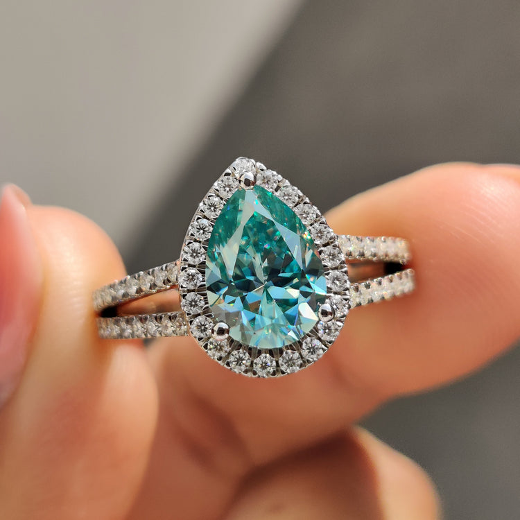 Pear cut engagement ring featuring cyan blue moissanite and round halo.