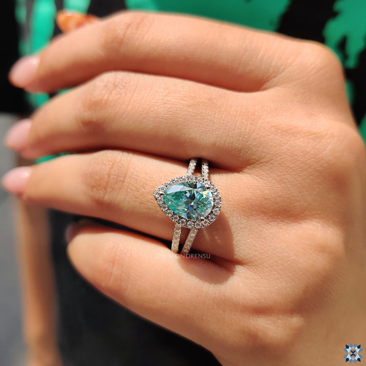 Cyan blue pear cut moissanite in a three-prong round halo setting.