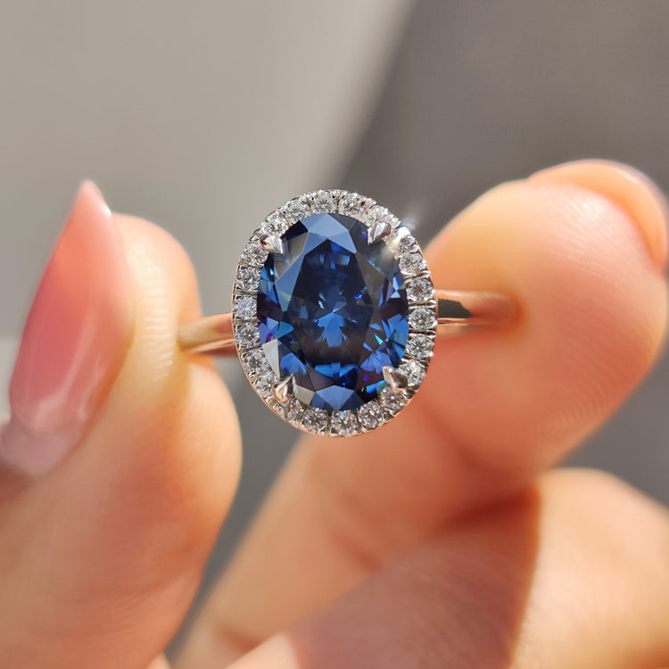 Oval cut dark blue moissanite engagement ring with round cut halo and cathedral setting.