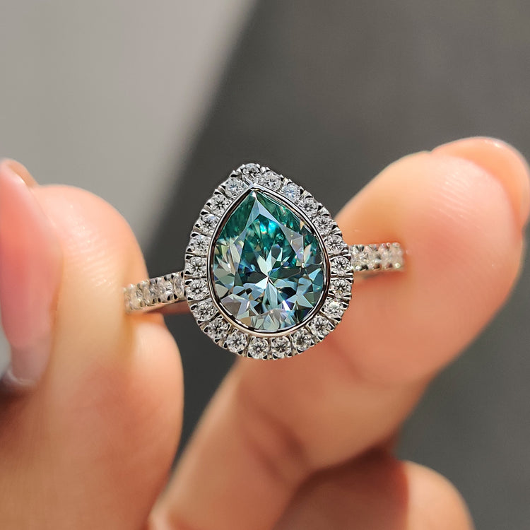 Cyan blue pear cut moissanite ring with round cut halo in white gold.
