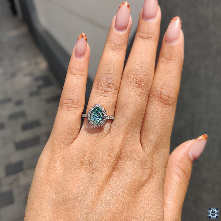 Handmade jewelry ring with cyan blue pear moissanite in halo setting.