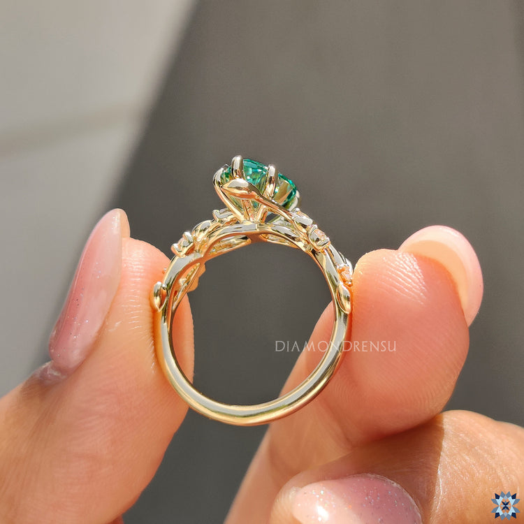 Pear cut moissanite ring with natural leafy design and vibrant green gemstone.