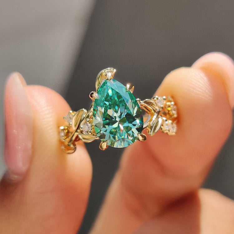 Pear cut engagement ring with green moissanite in a yellow gold nature-inspired design.