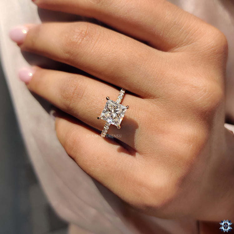 Elegant princess cut Moissanite ring with pave band and yellow gold shank.