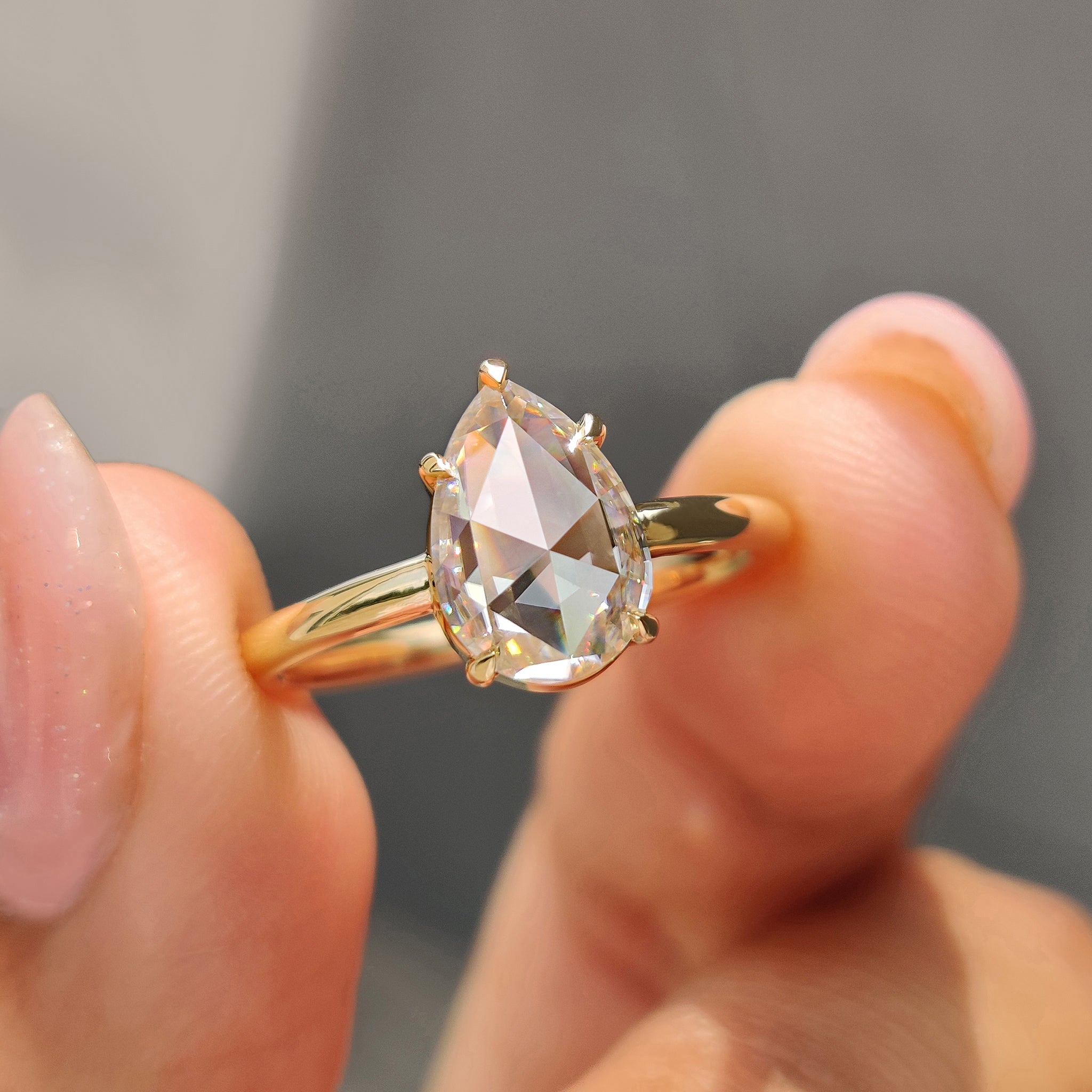 Gold solitaire engagement ring featuring pear rose cut Moissanite and 5 claw prong setting.