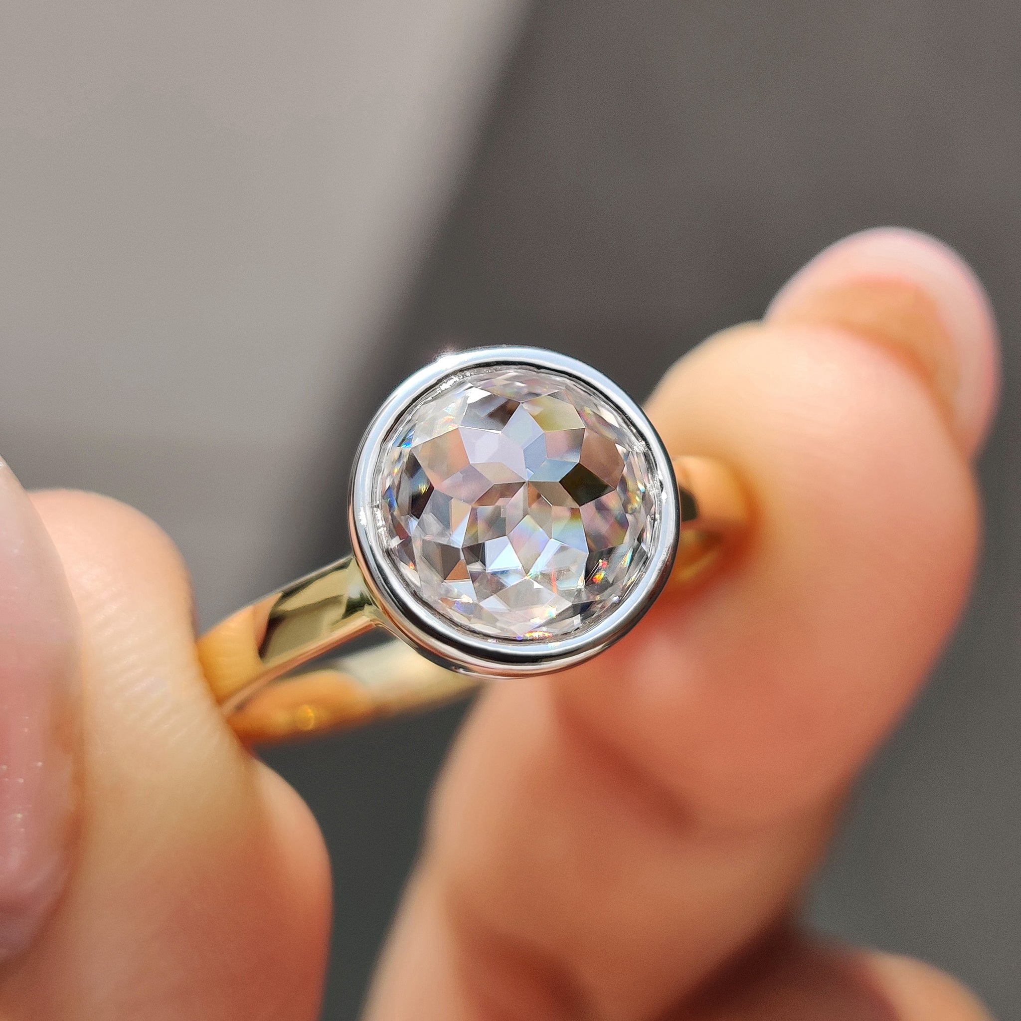 Bezel engagement ring with round rose cut Moissanite in two-tone gold setting.