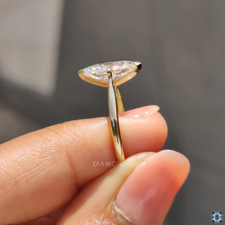 Yellow gold moissanite solitaire ring with V prong and tapered shank band.