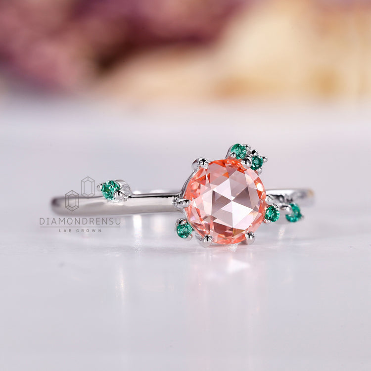 Peach sapphire cluster ring with emerald accents and prongs.