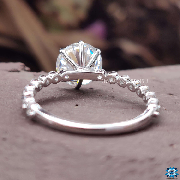 Shared prong band ring with round moissanite and pave set side stones.
