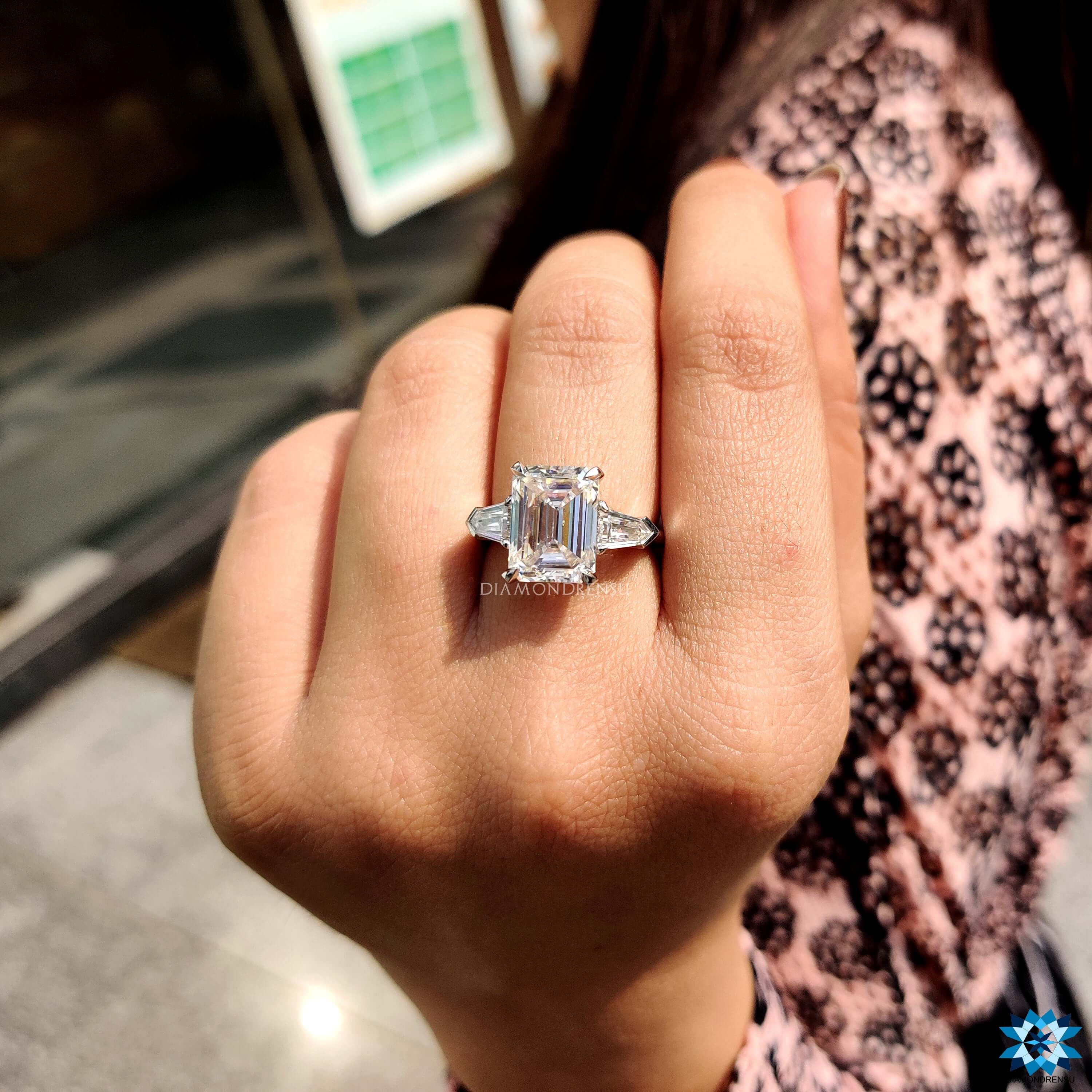 White gold three stone ring featuring emerald center and bullet cut accents.