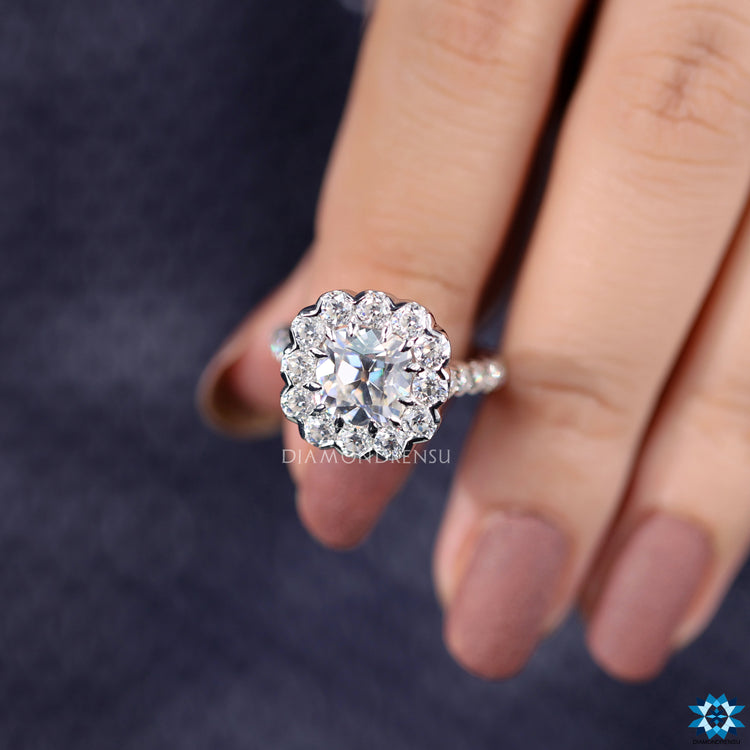 Halo engagement ring featuring cushion moissanite and round cut halo accents.