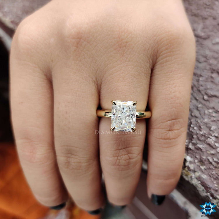 Four prong yellow gold ring with radiant moissanite centerpiece.