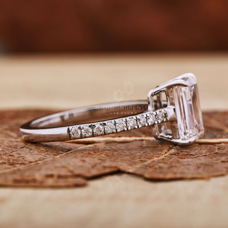 Emerald engagement ring in a classic claw prong setting, accented with Round Cut Diamond Side Stones for added sparkle.