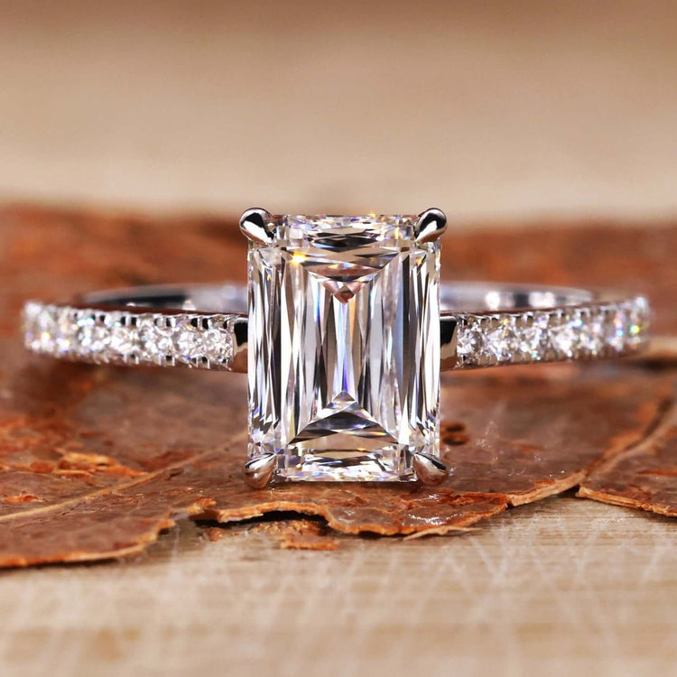 Emerald and diamond engagement ring featuring a 4 prong claw setting and elegant pave diamonds for timeless beauty.
