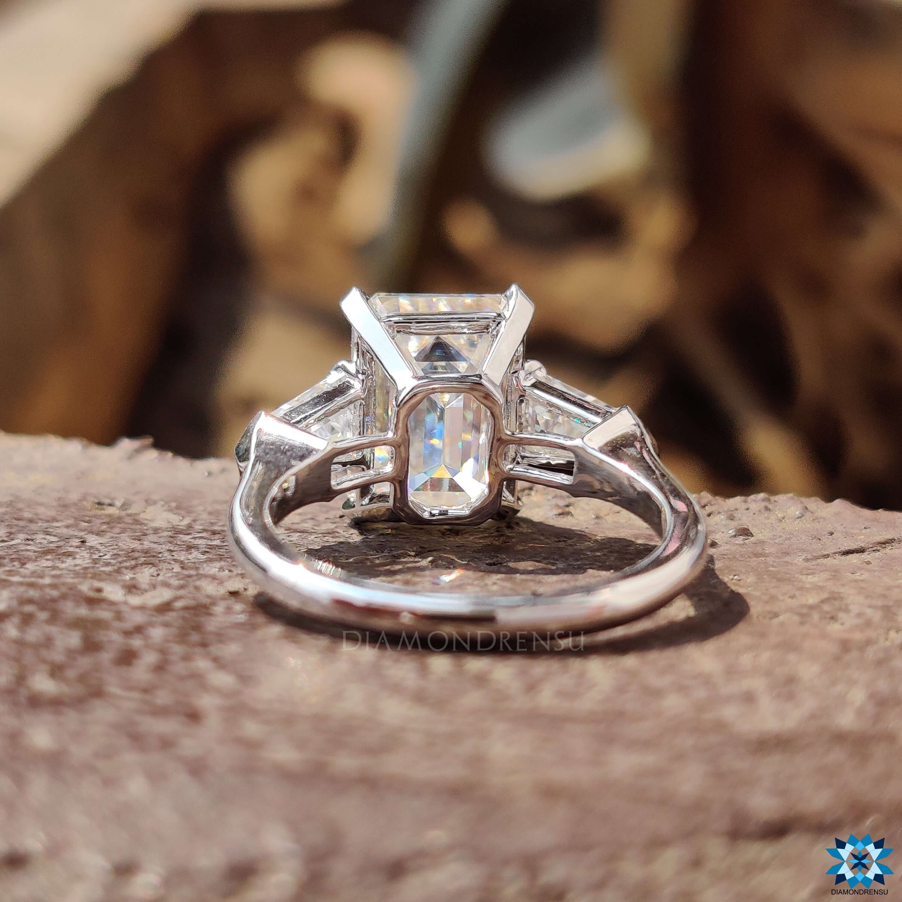 Emerald cut moissanite ring with prong setting and side bullet cuts.