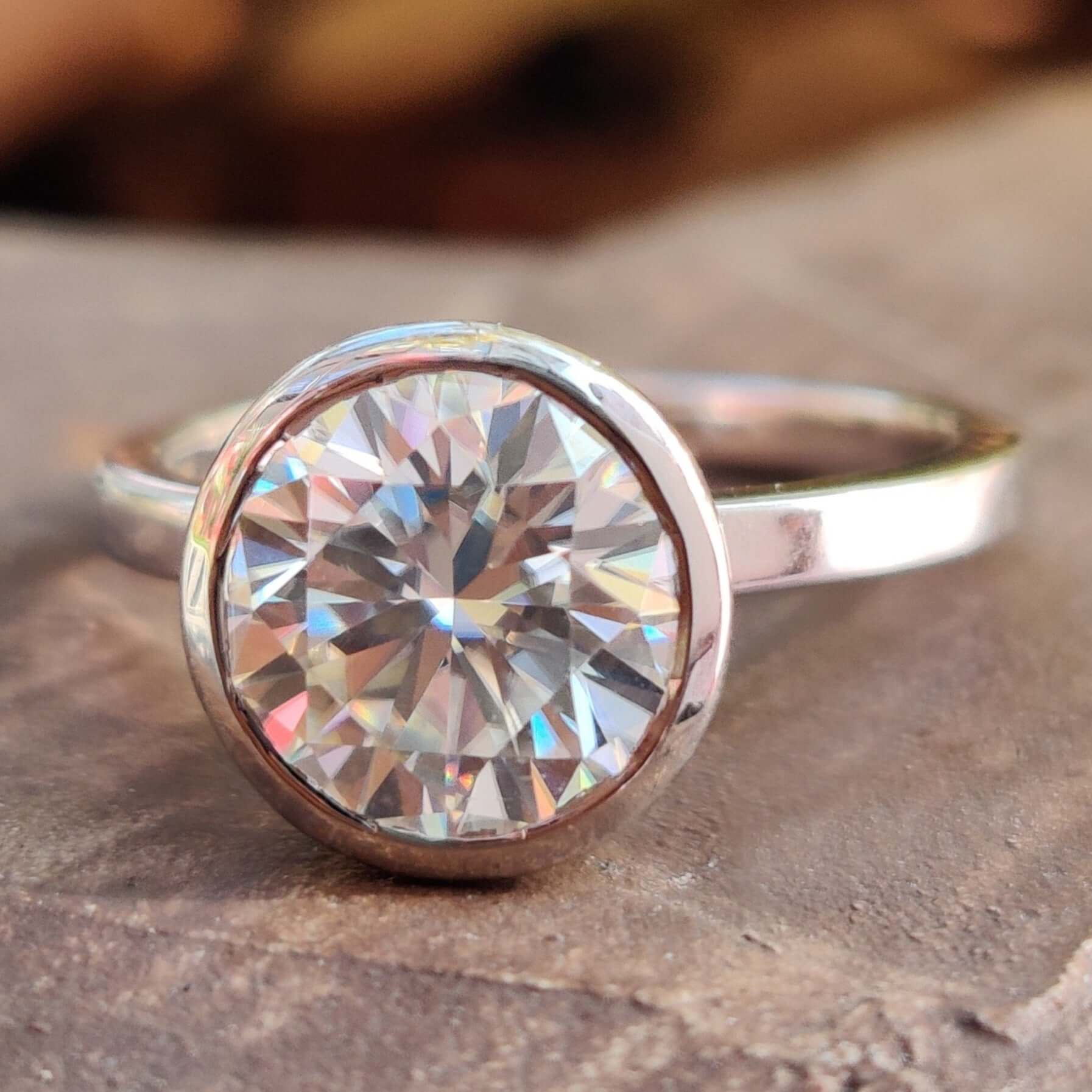 Engagement ring with bezel setting featuring round Moissanite in elegant white gold.