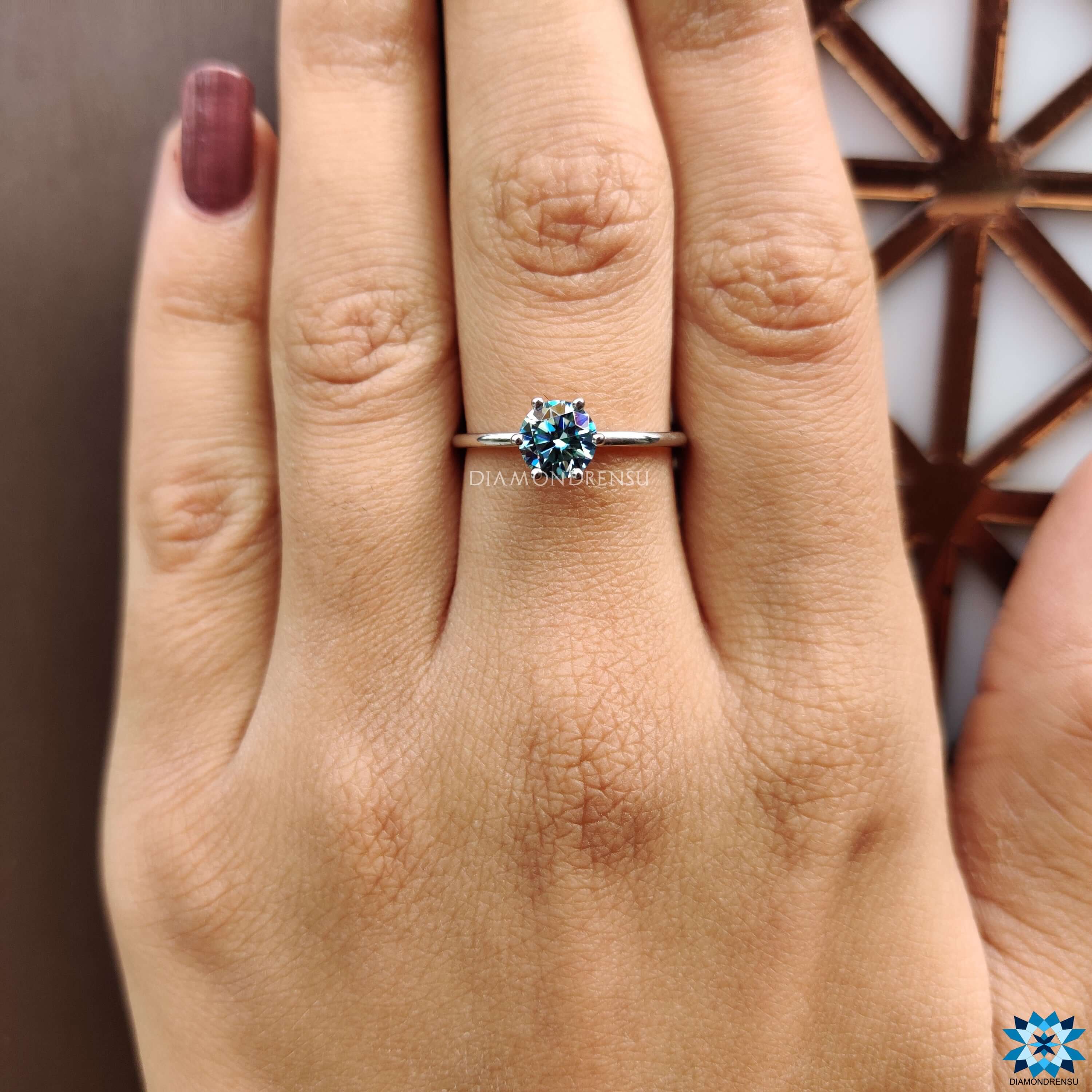 Round moissanite ring with cyan hue in prong setting.