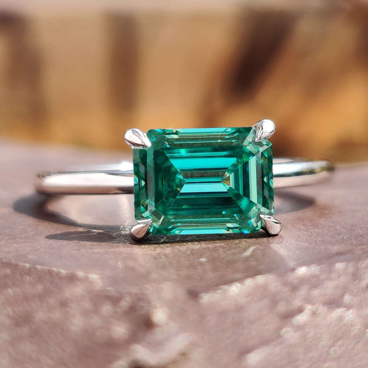 Green moissanite emerald cut ring in east west setting.