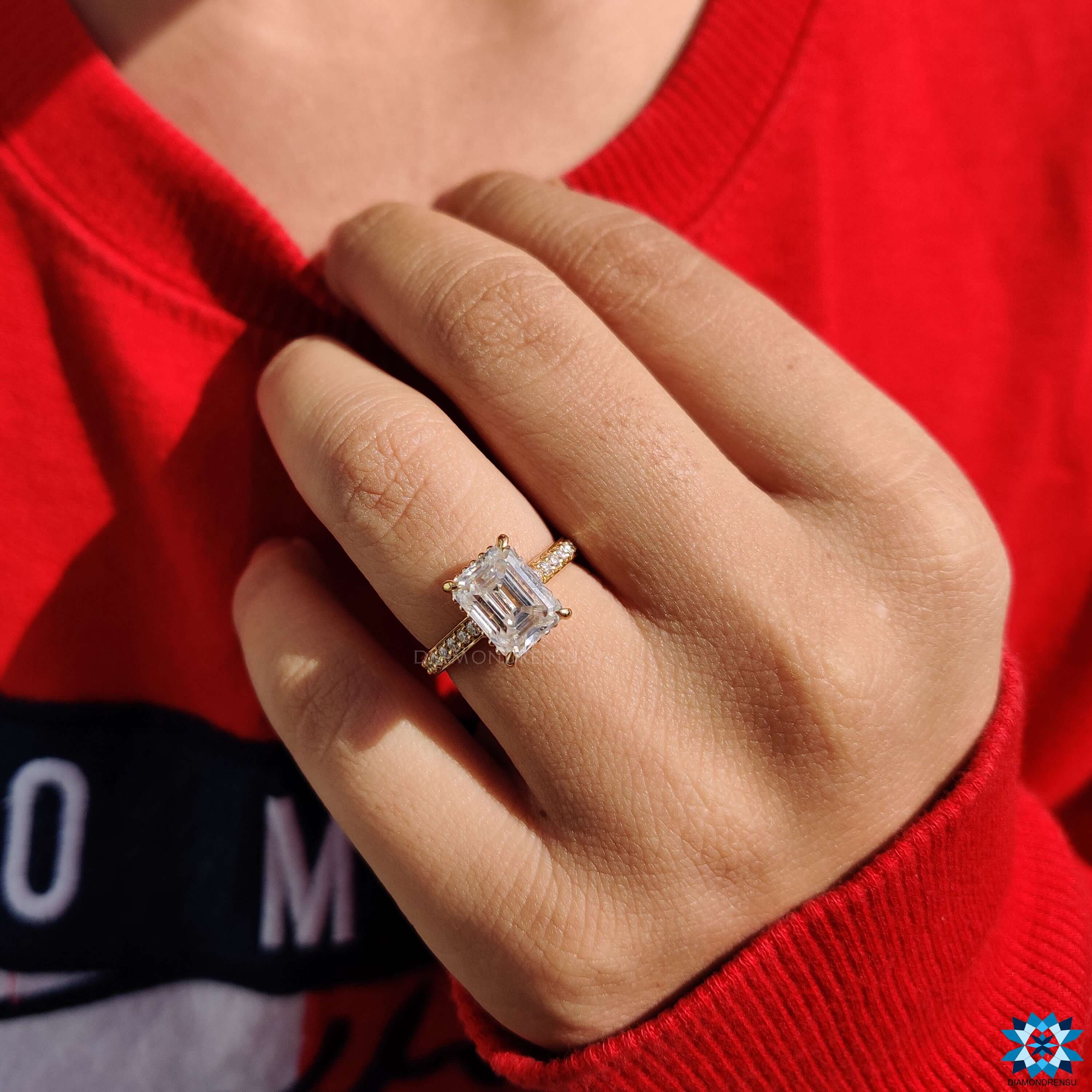 4 claw prong setting secures emerald cut moissanite in a yellow gold band.