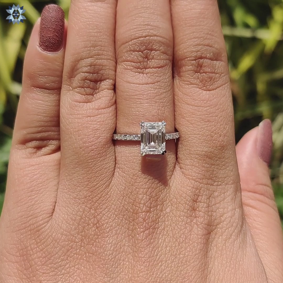 Prong set emerald cut moissanite ring designed with a pave band.