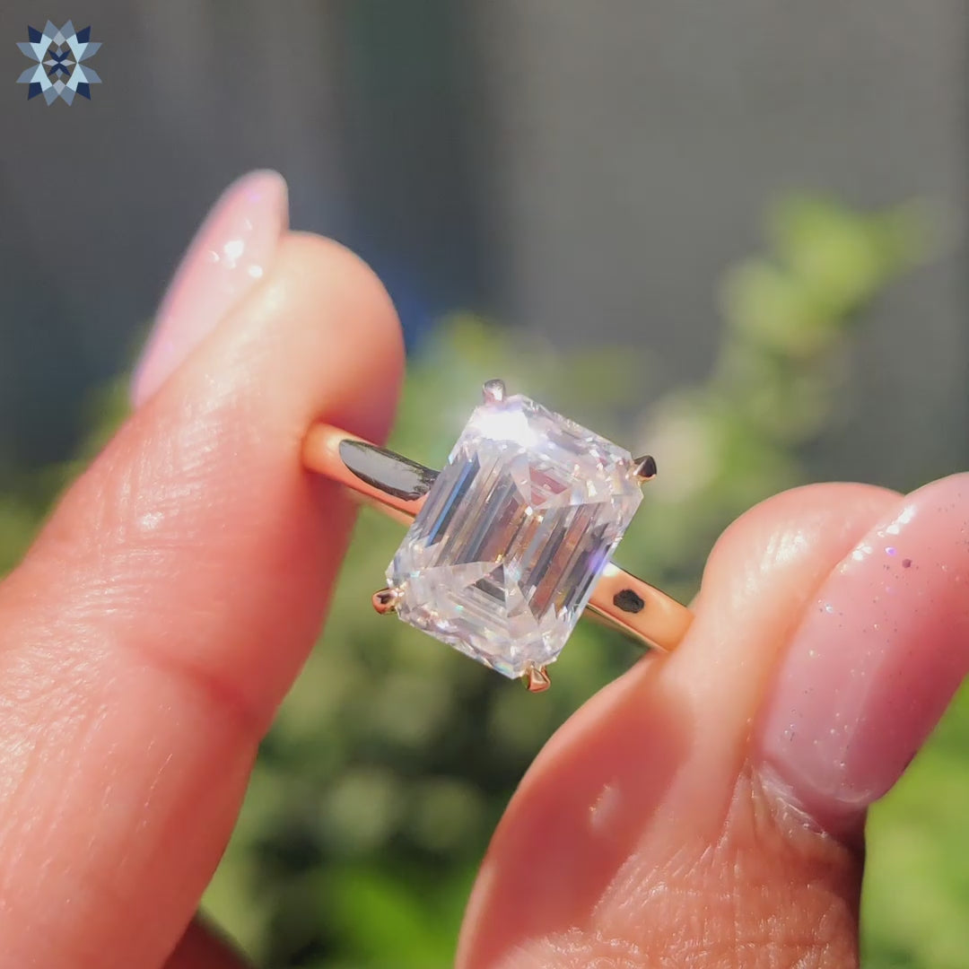 Simple moissanite engagement ring featuring emerald cut stone and cathedral setting.