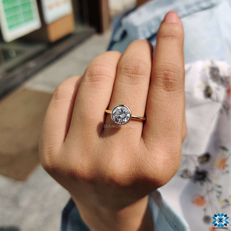 Bezel set solitaire ring with round moissanite in yellow gold.