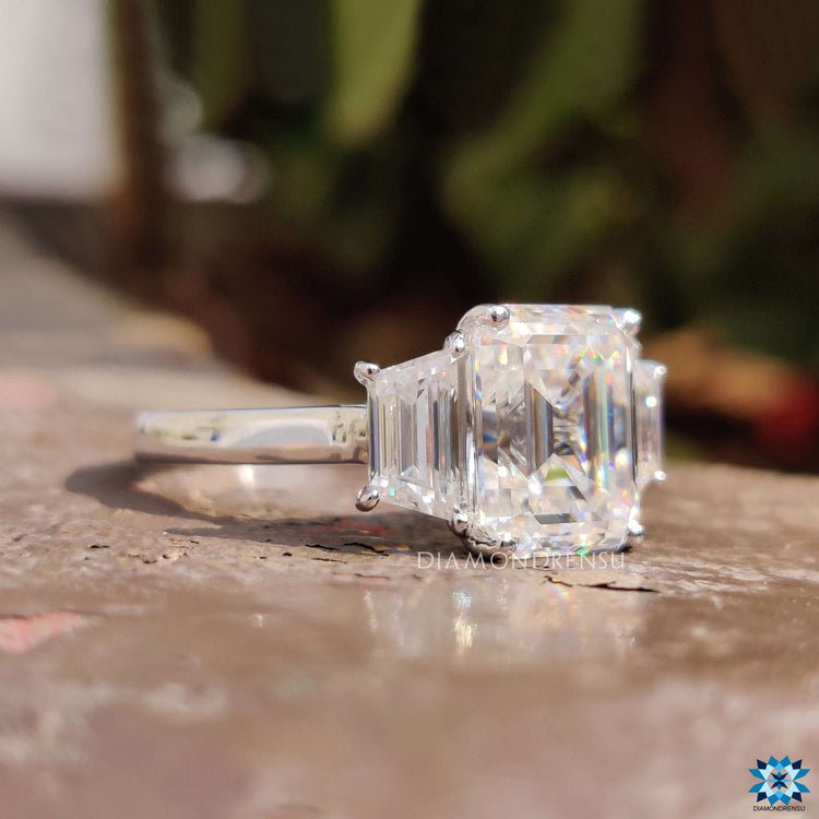 Trapezoid side stone ring featuring a moissanite emerald centre in white gold.