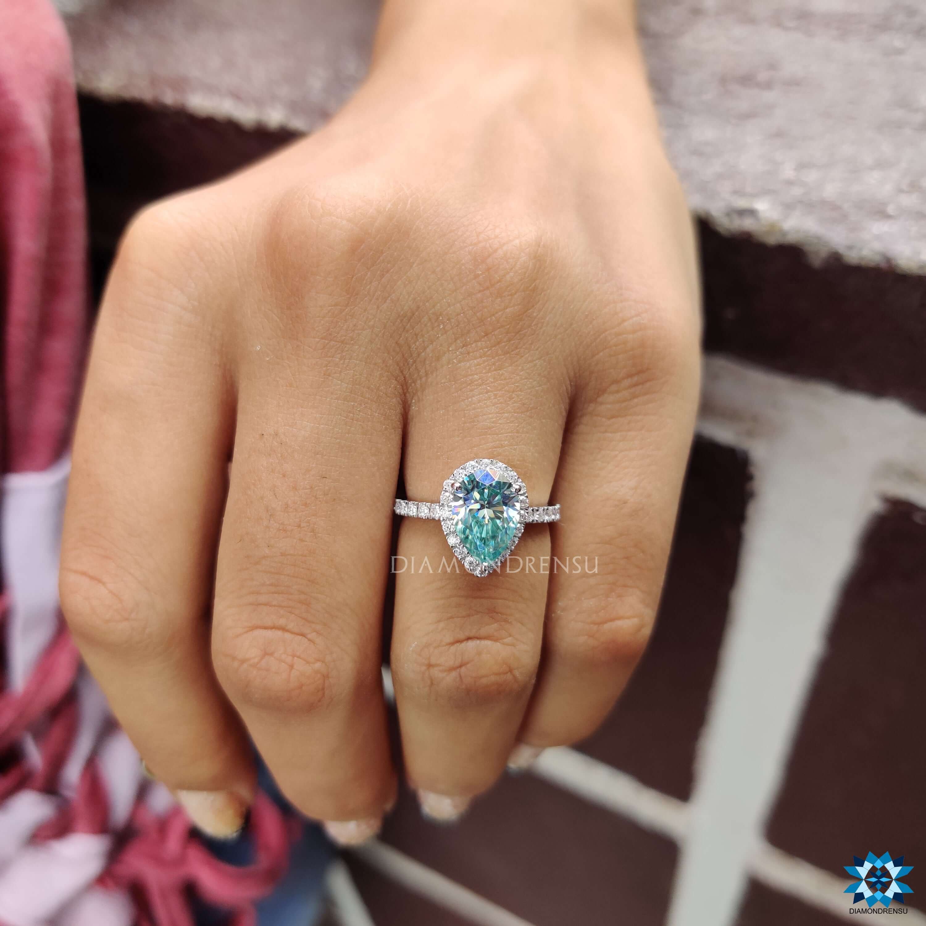 Moissanite halo ring featuring a cyan blue pear cut stone in prong setting.