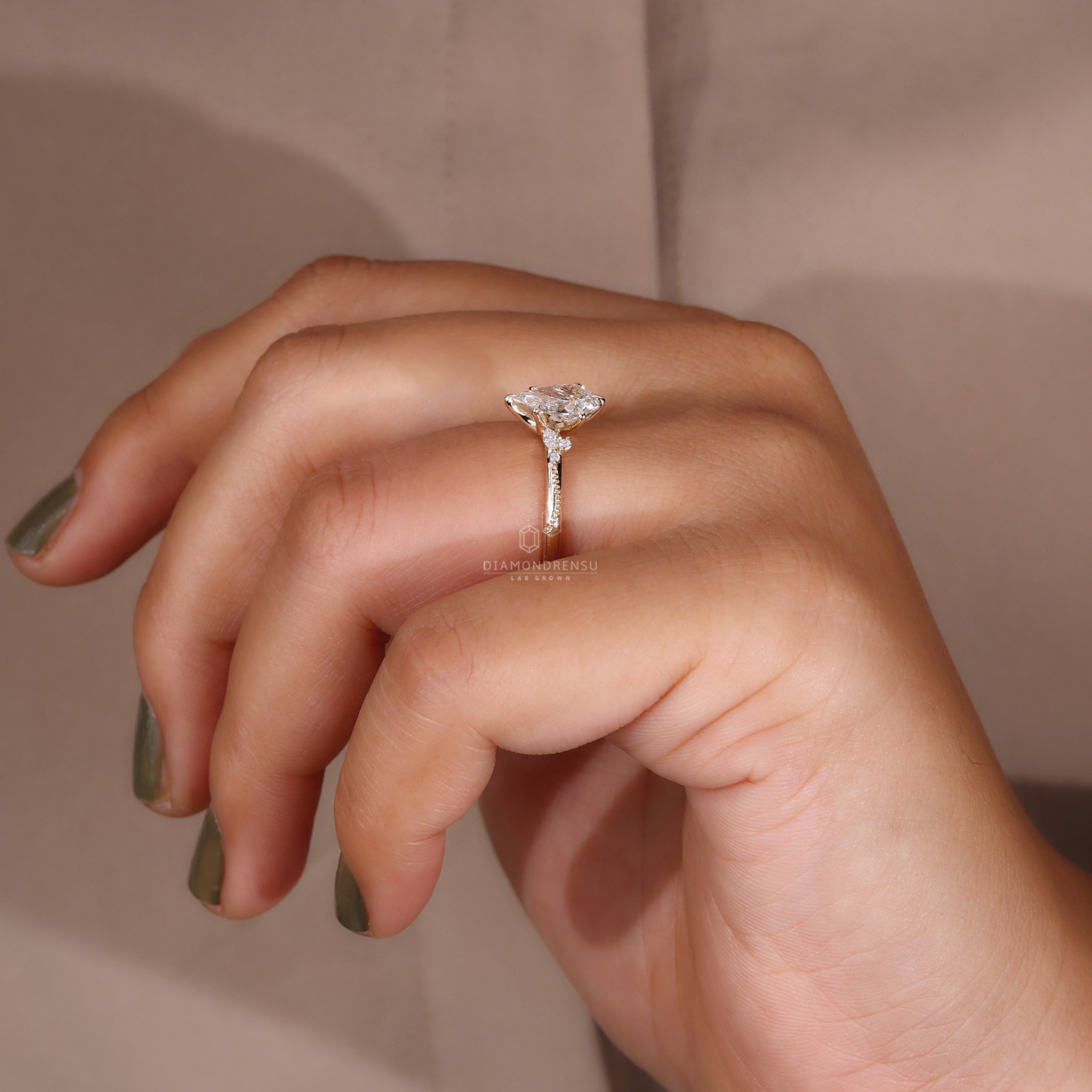 Pear cut diamond ring with marquise sidestone and miligrain design on a model's finger.