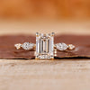 5 stone engagement ring with emerald center diamond and yellow gold setting.
