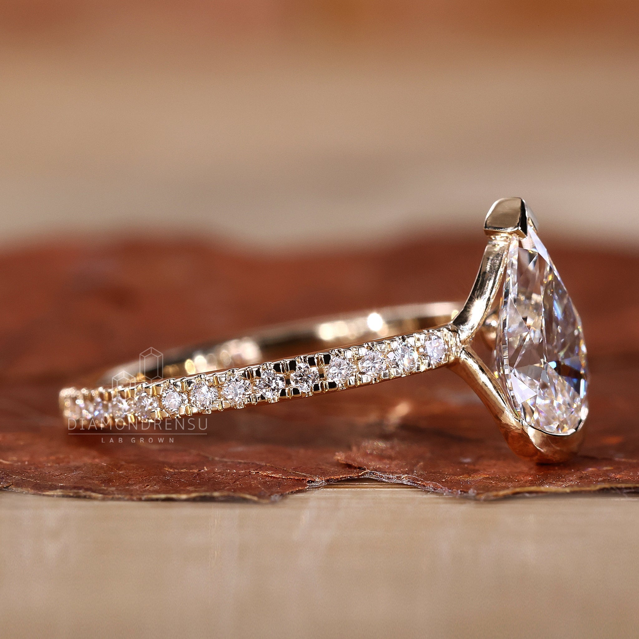 A beautifully crafted lab created diamond engagement ring with a pear cut diamond in a half bezel setting.