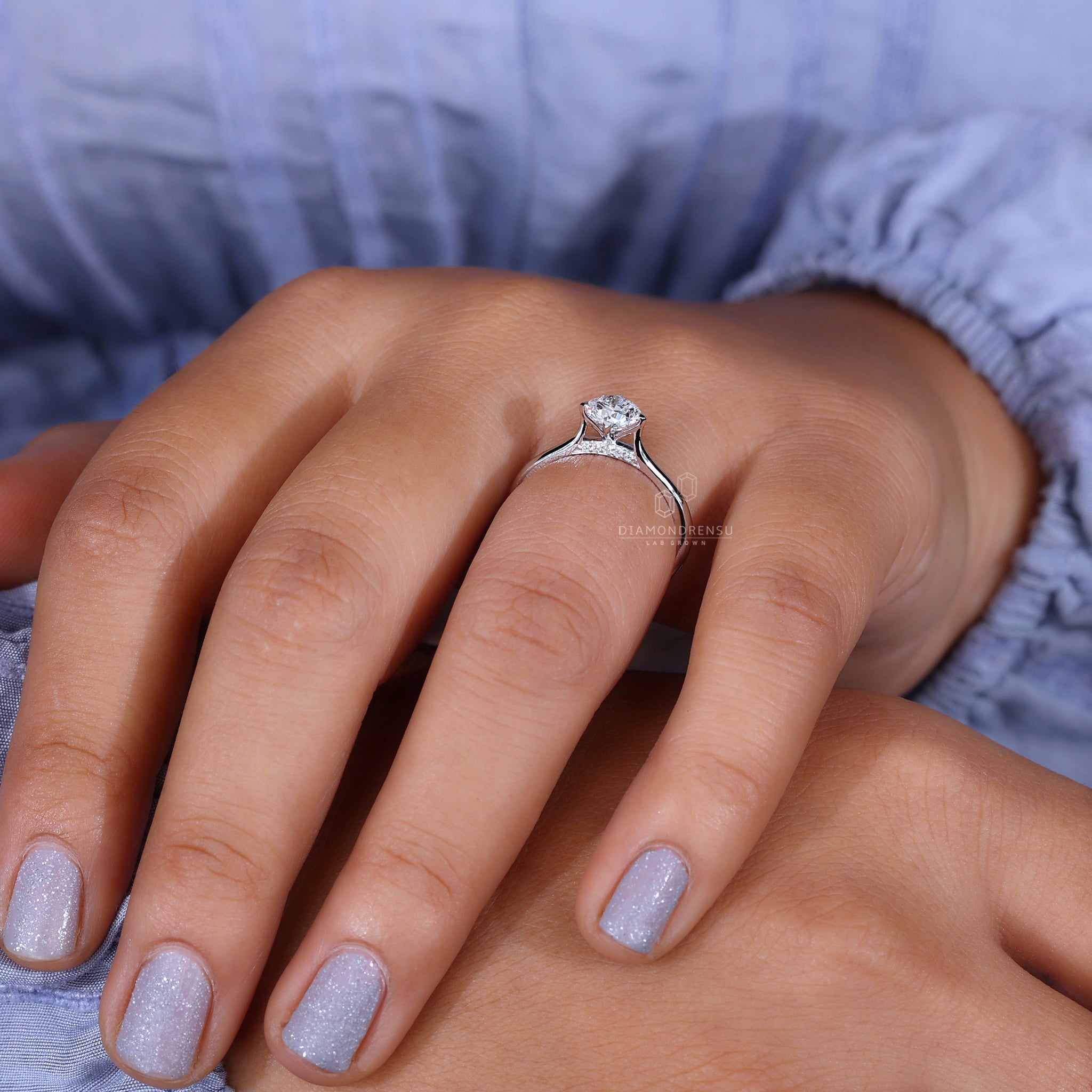 Round solitaire engagement ring with diamond bridge accent on model's hand