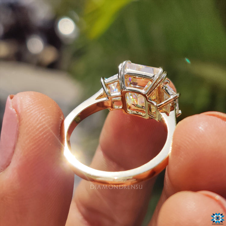 UK engagement ring featuring emerald cut moissanite and yellow gold band.
