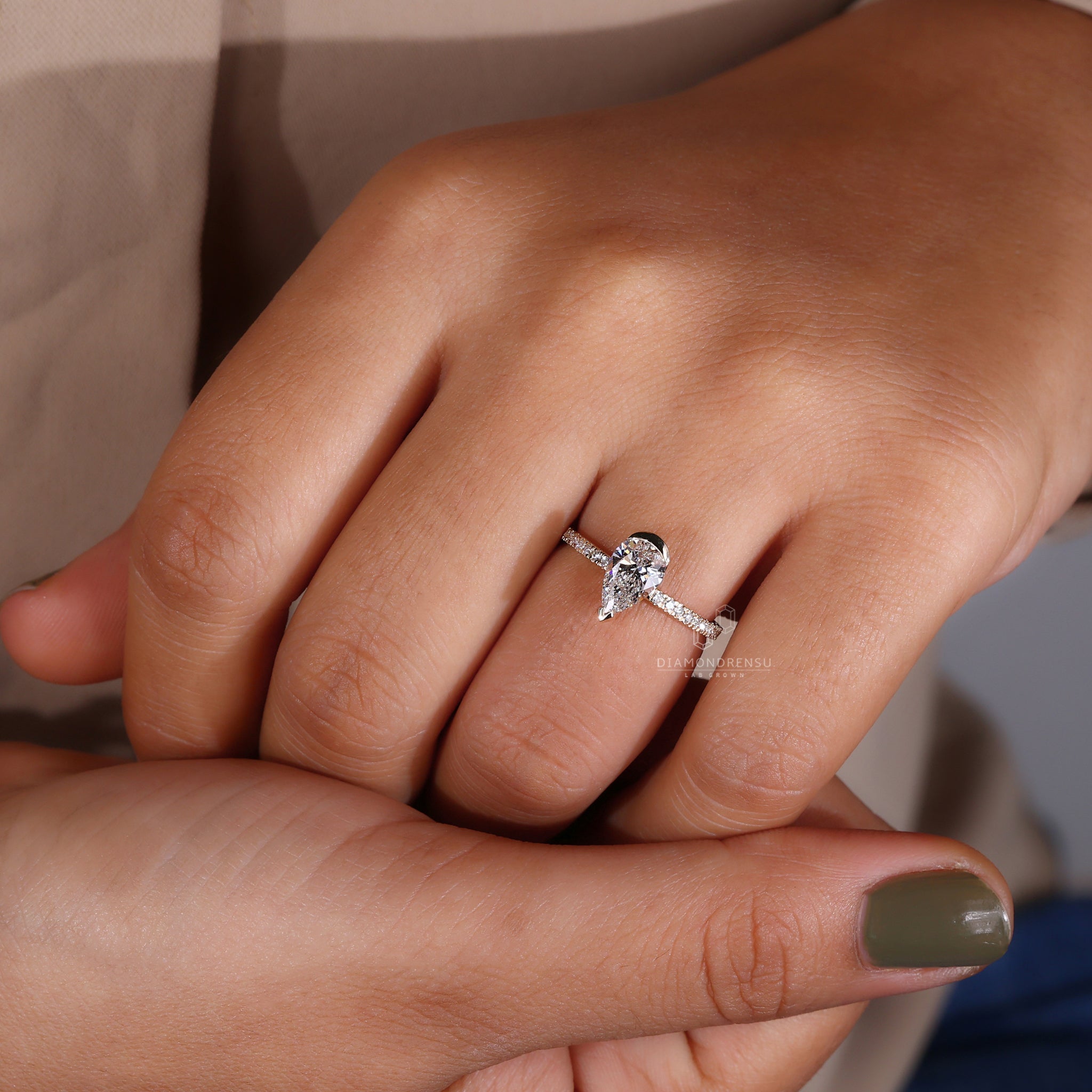 A model's hand adorned with a pear shaped ring featuring a pear cut diamond in a half bezel setting, made of yellow gold.