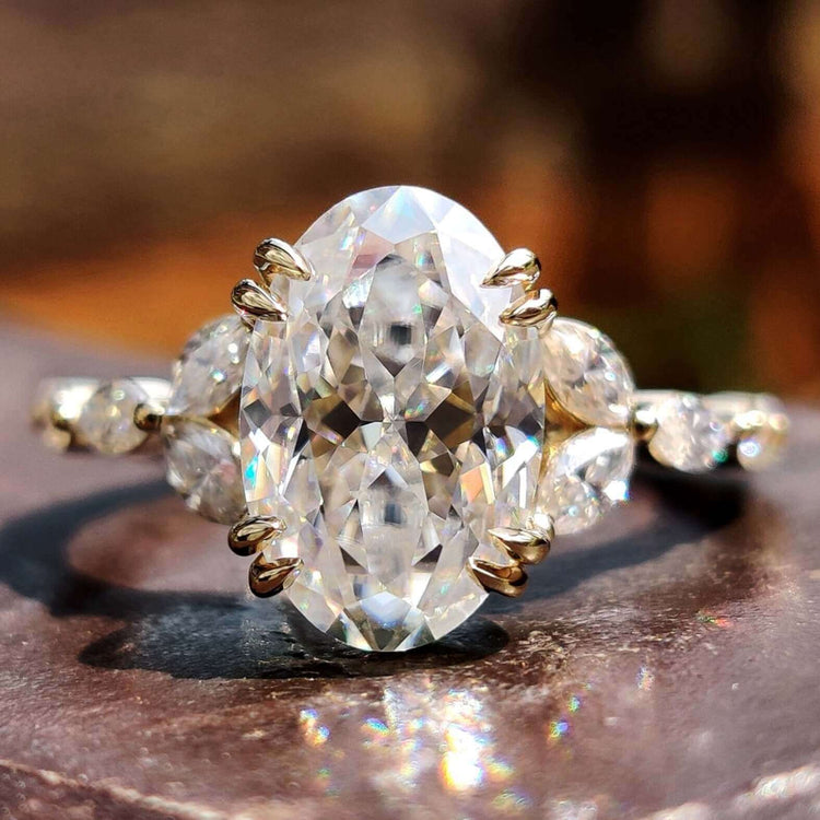 Oval Rensu cut moissanite engagement ring with marquise and round side stones.

